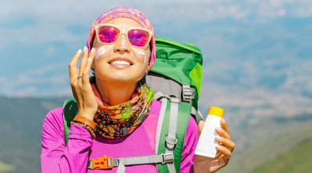 woman_hiking_mountains_backpack_using_sunscreen_AdobeStock_237235761.6776cb126cc68.png